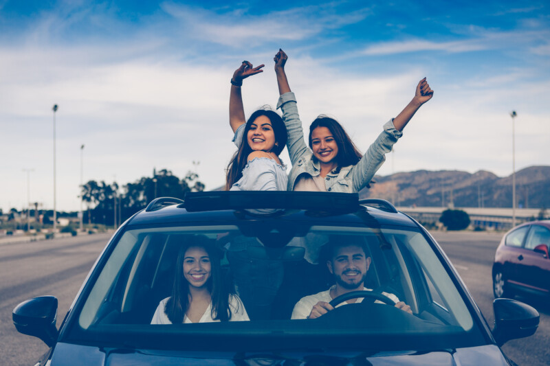 Two girls friends with a freedom position with their arms raised through the top window of a car during a travel with friends